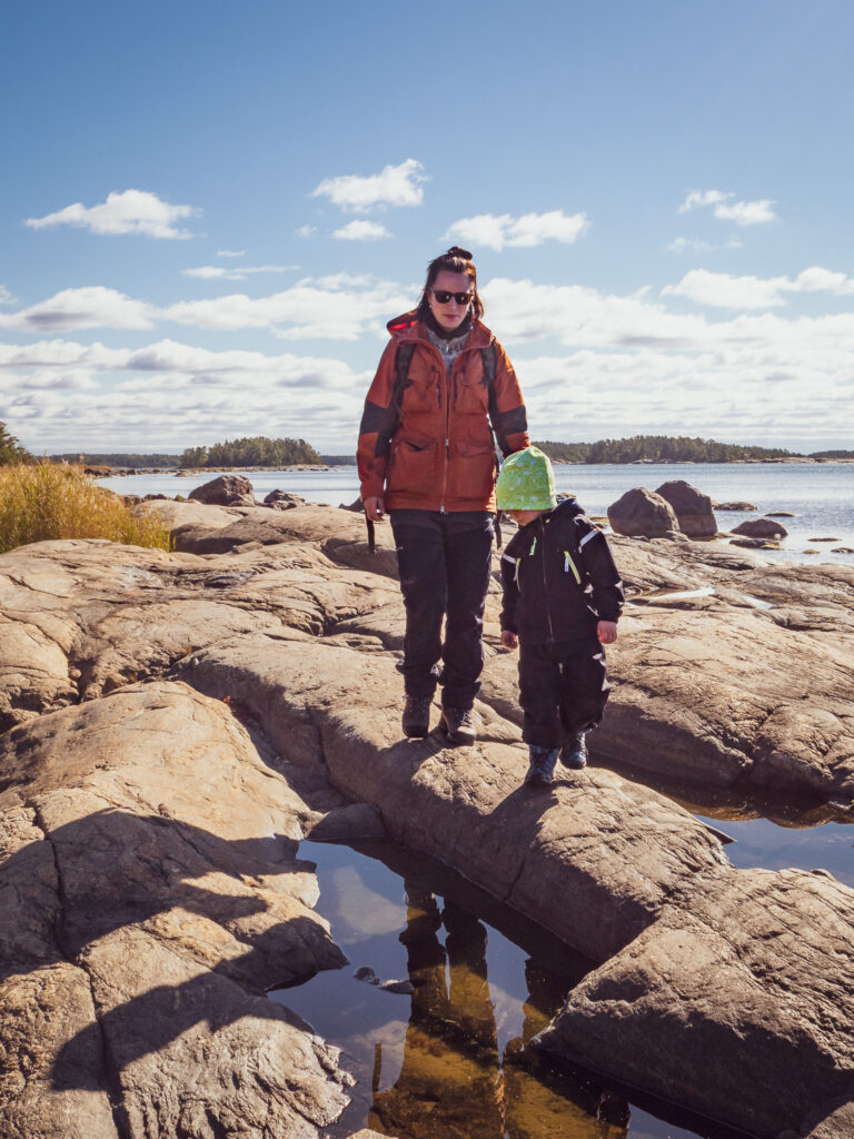 Ihmisiä saaristossa kävelemässä kallion päällä, merta taustalla.