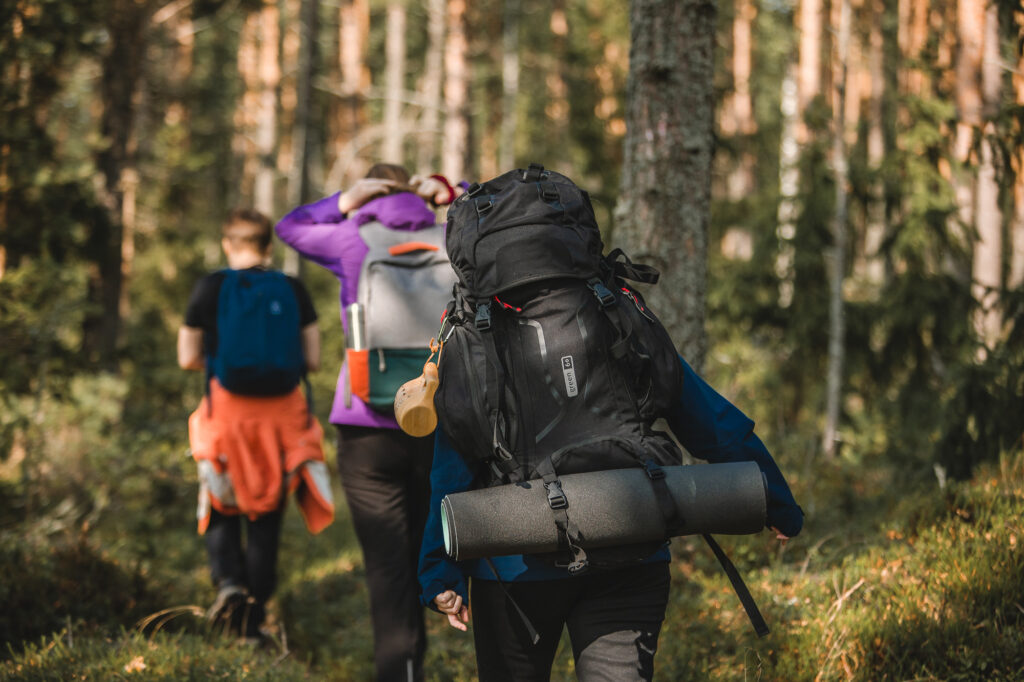 Kolme ihmistä patikoimassa metsässä reput ja rinkat selässä.