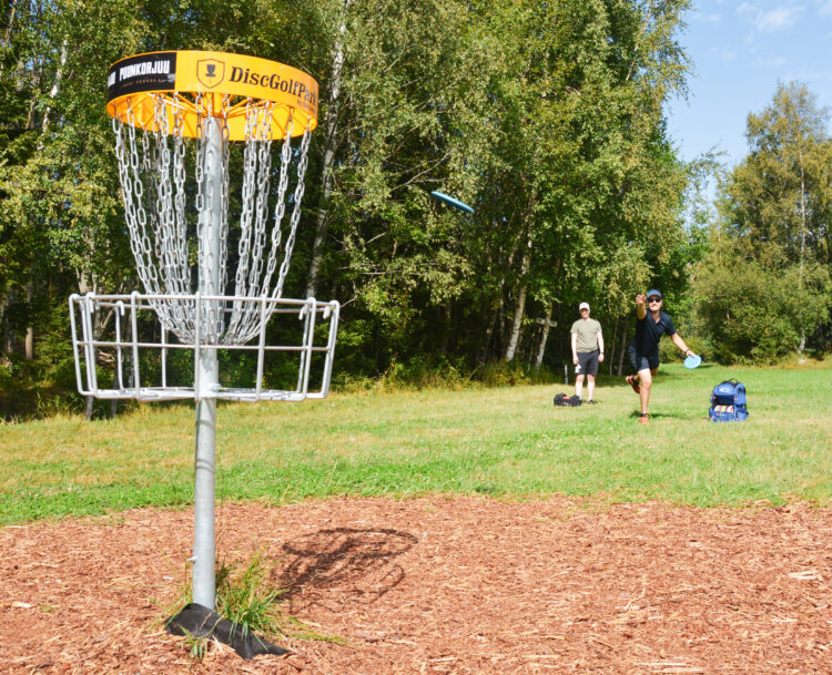 Frisbeegolf pelaajia heittämässä frisbeen koriin.