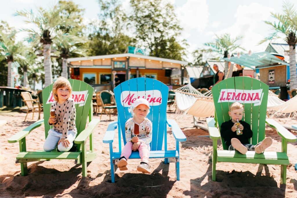 Three kids sitting on beach chairs eating ice cream.