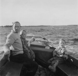 Kuva vuodelta 1956, jossa veneessä istuvat isä ja kaksi pientä poikaa.
